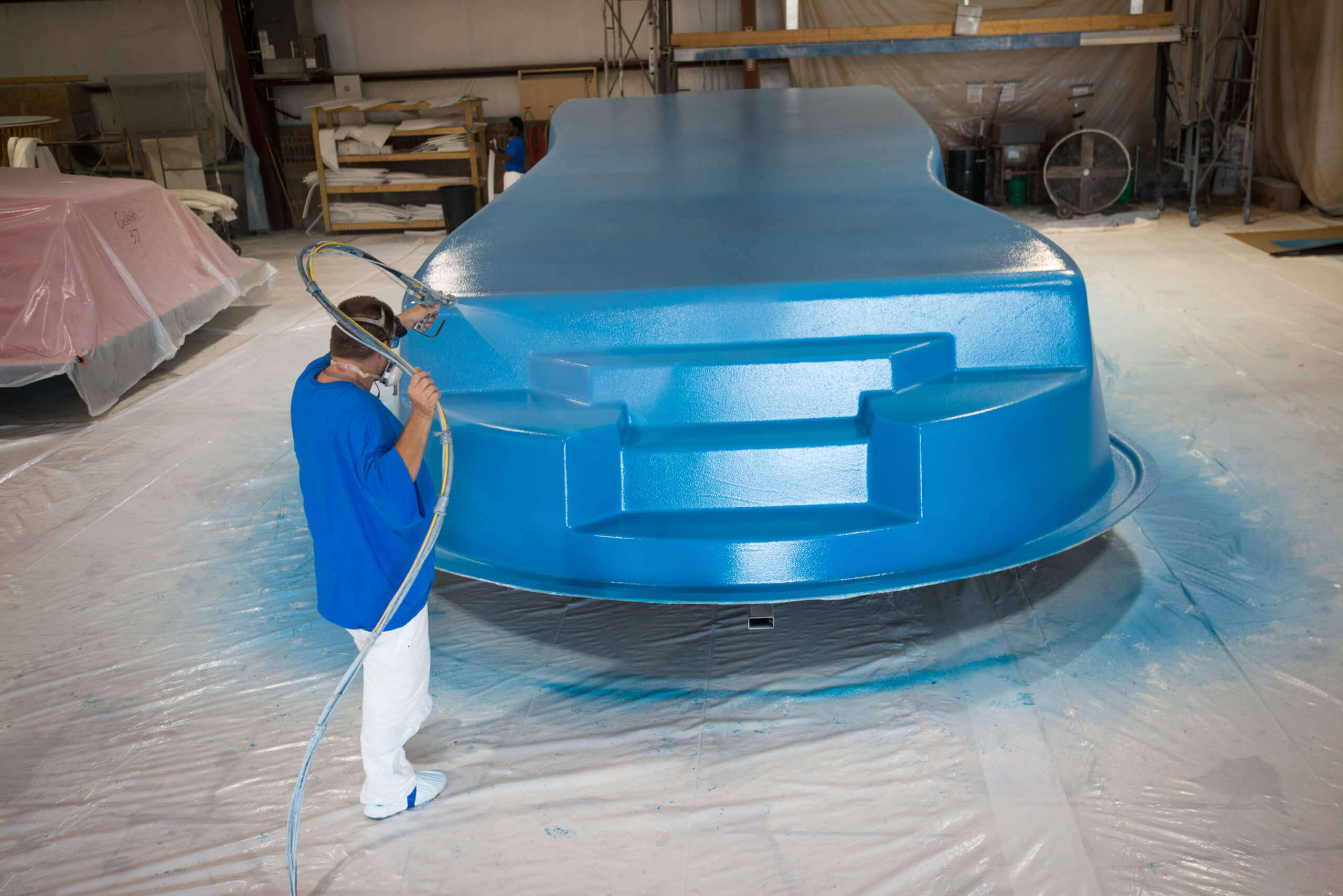 Thursday Pools worker spraying pool with blue paint in warehouse
