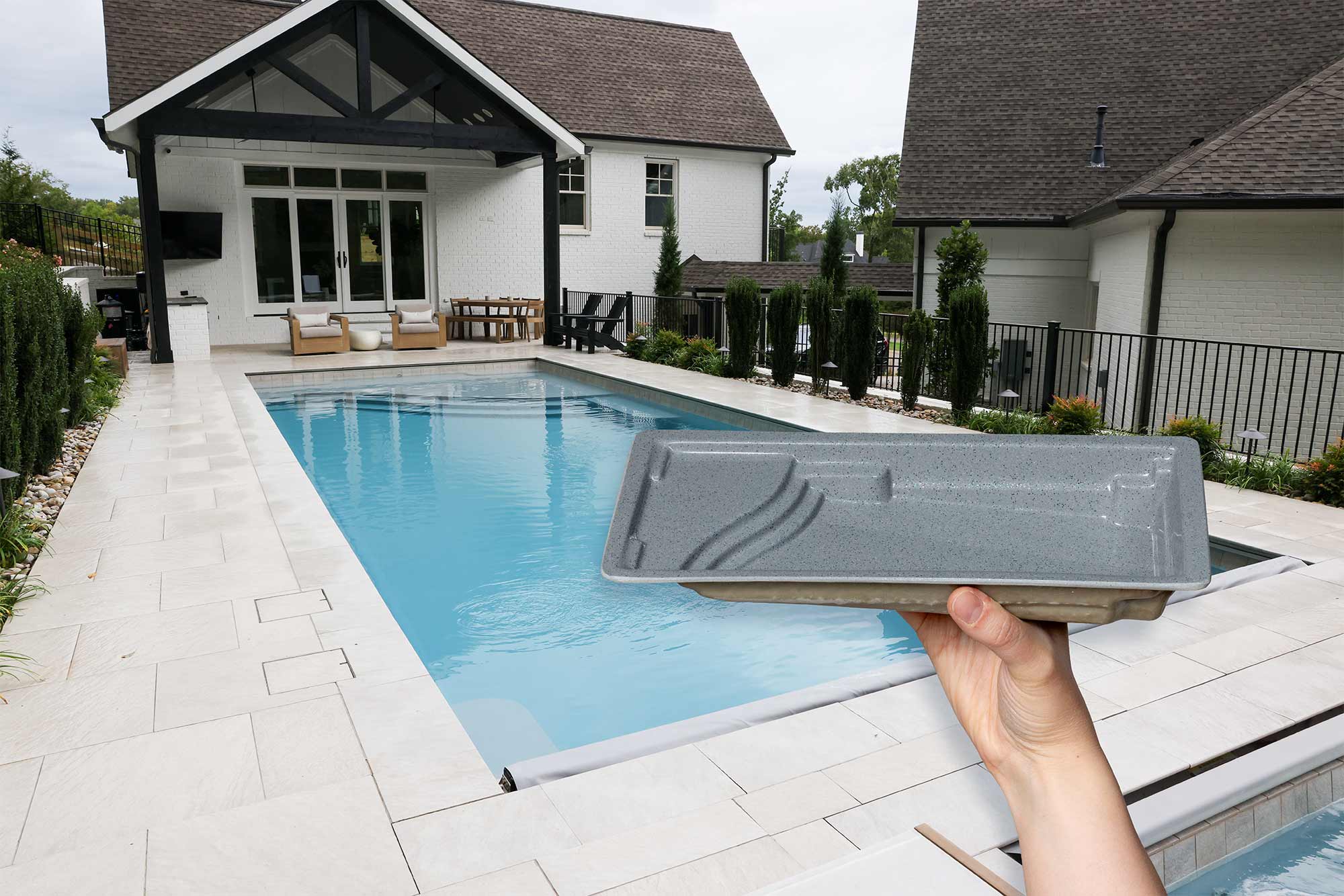 hand holding a pocket sized pool model of an Aspen by Thursday Pools in front of a beautifully installed Aspen pool