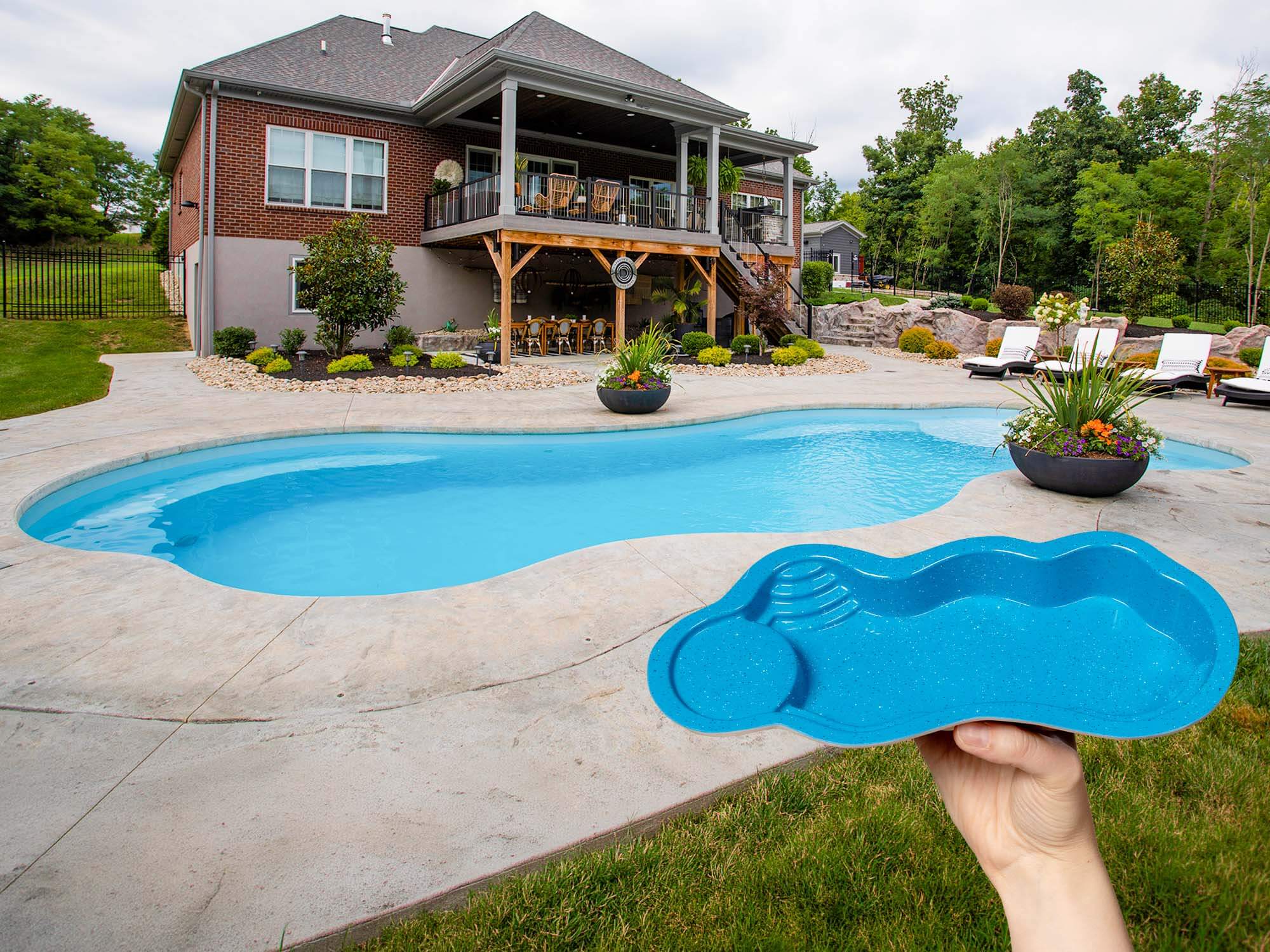 hand holding a pocket sized pool model of an Aspen by Thursday Pools in front of a beautifully installed Aspen pool